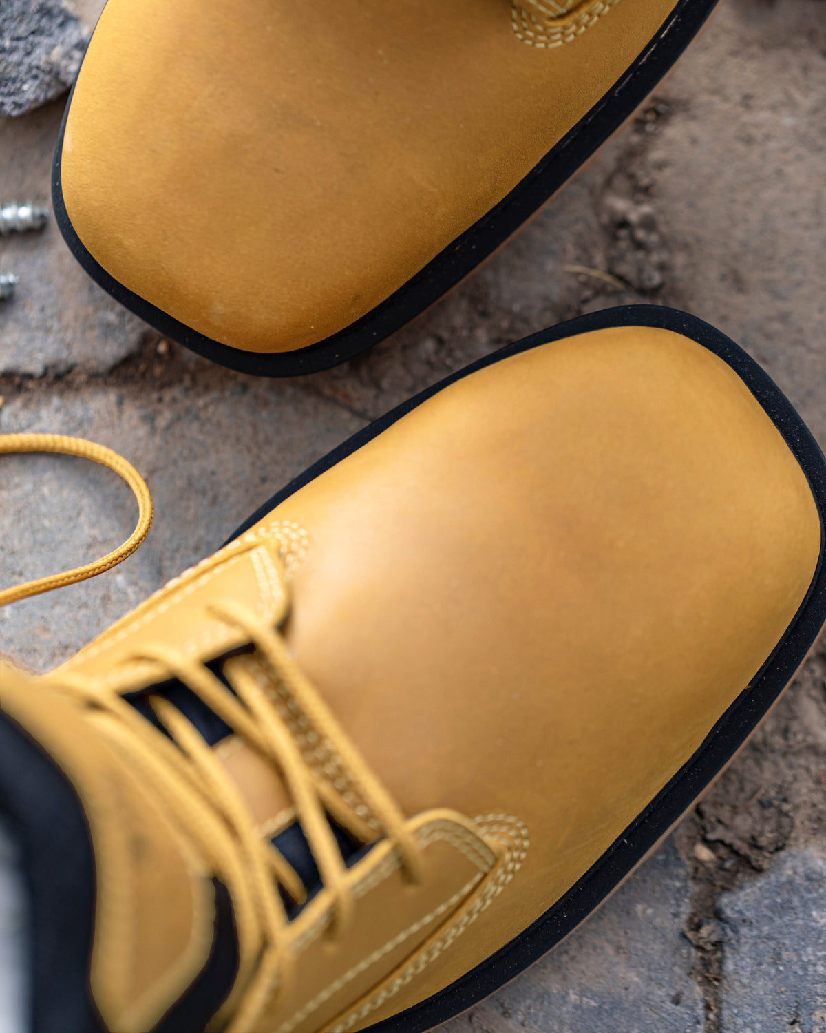 Close-up of a pair of yellow leather work boots with black soles, resting on a rough concrete surface.