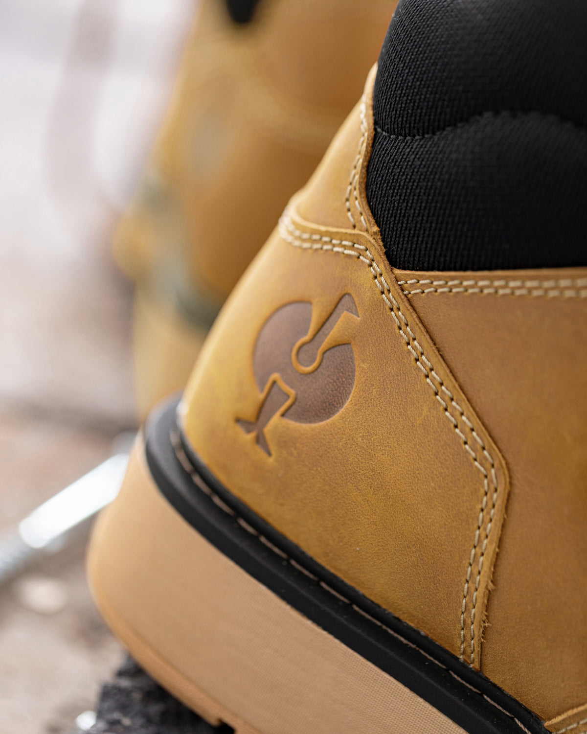 Close-up of a tan suede high-top shoe with a black sock inserted, showing a debossed logo on the heel and a thick tan sole.