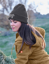 Woman wearing a dark grey beanie and brown jacket outdoors