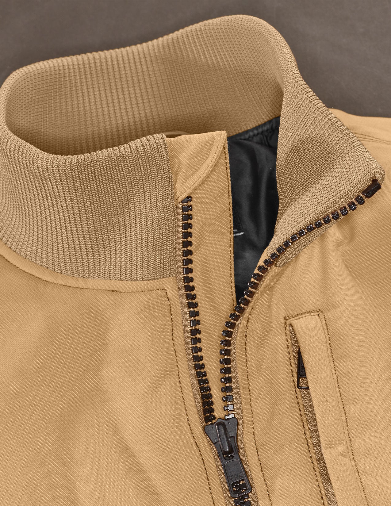 Close-up of a tan jacket with a zipper and black interior lining.