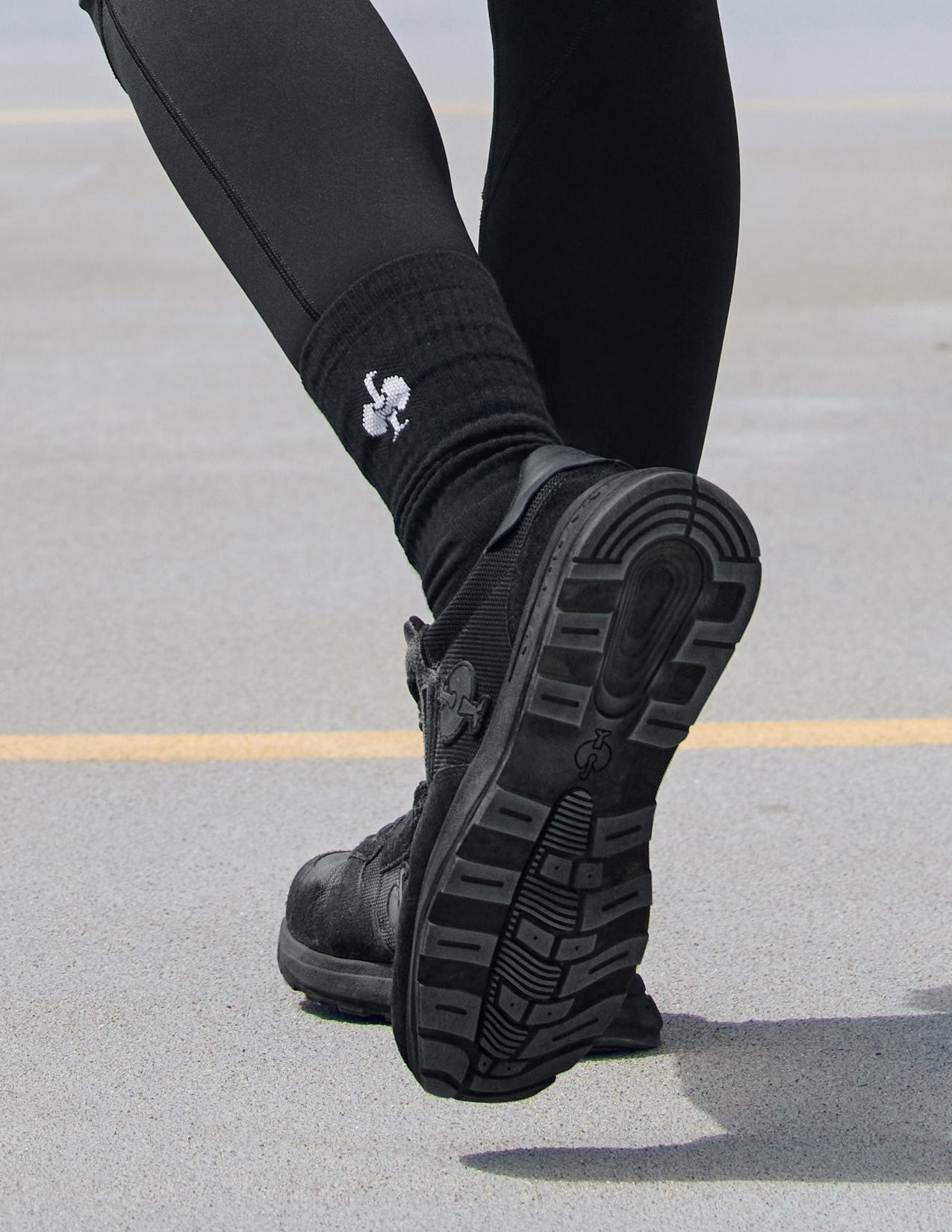 Black boots with a brand logo worn on a gray pavement surface