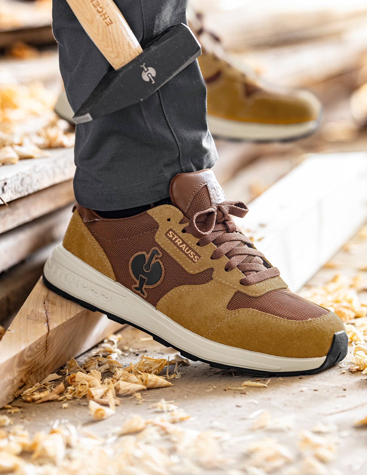 Brown and tan sneaker with Strauss brand logo on a wooden floor background