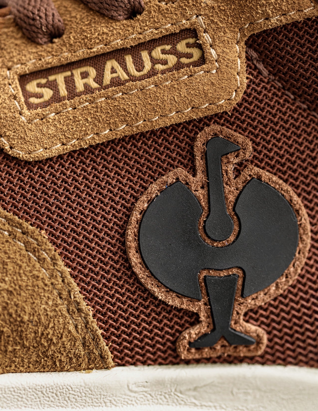 Close-up of a brown shoe with 'Strauss' branding and a logo on the side.