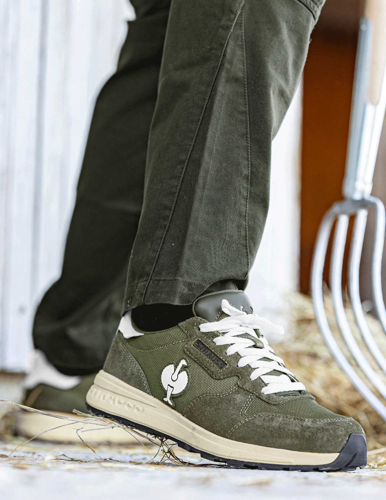 Green sneakers with a brand logo worn with dark pants on a neutral background