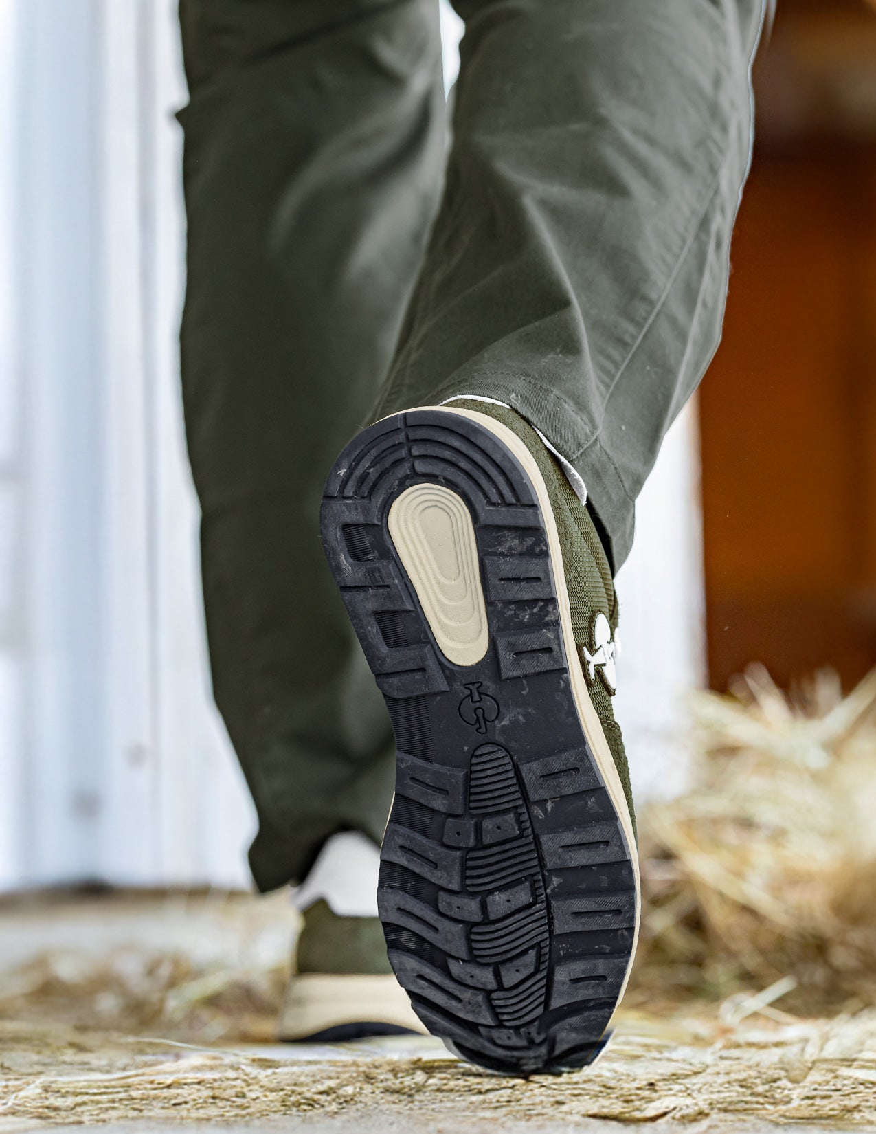Close-up of a person wearing green shoes with a textured sole on a wooden floor.