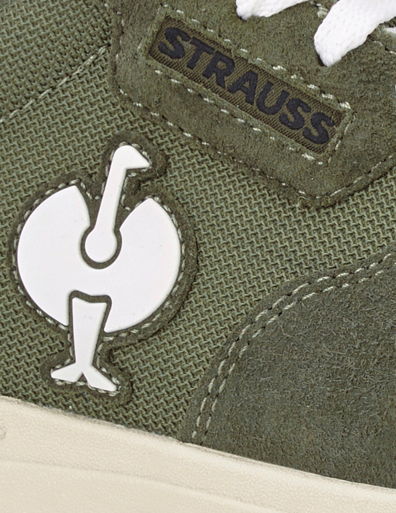 Close-up of a green shoe with 'Strauss' branding and logo.