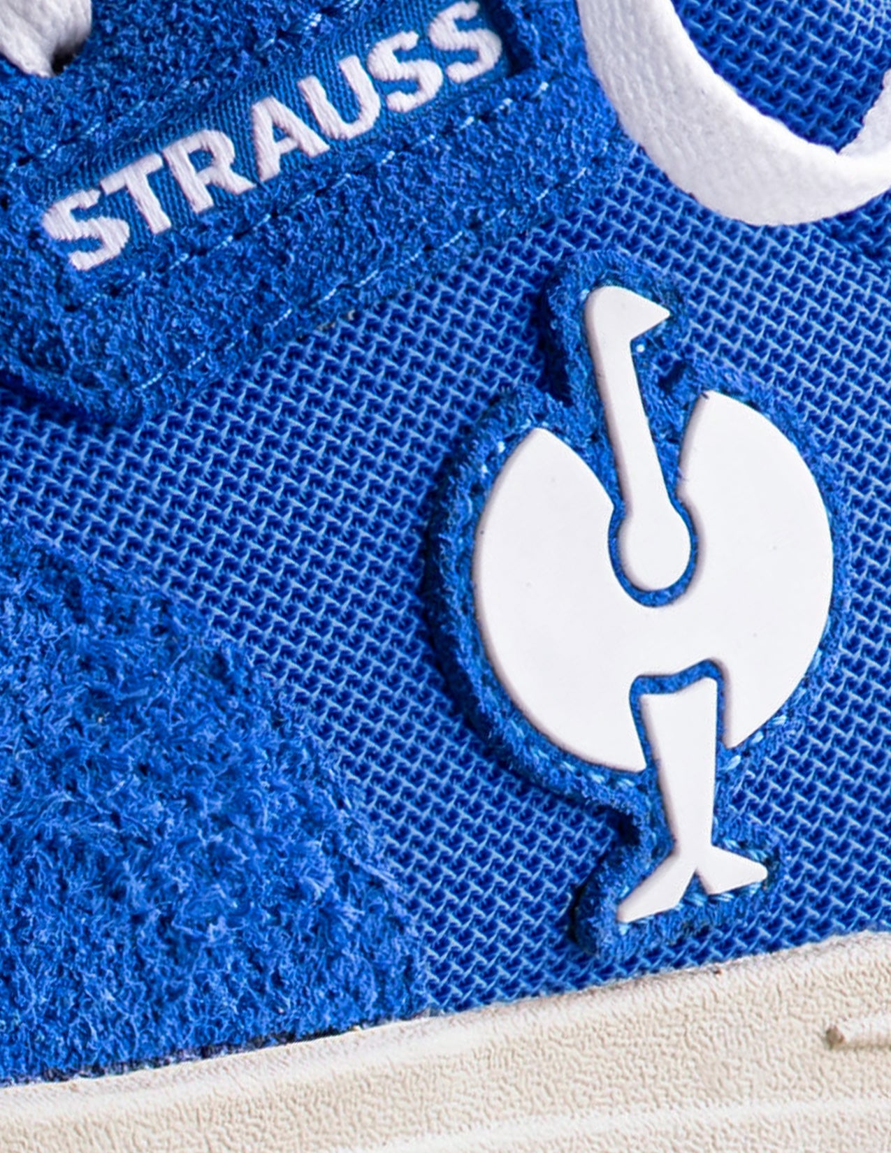 Close-up of a blue shoe with 'STRAUSS' branding and a logo on a white background