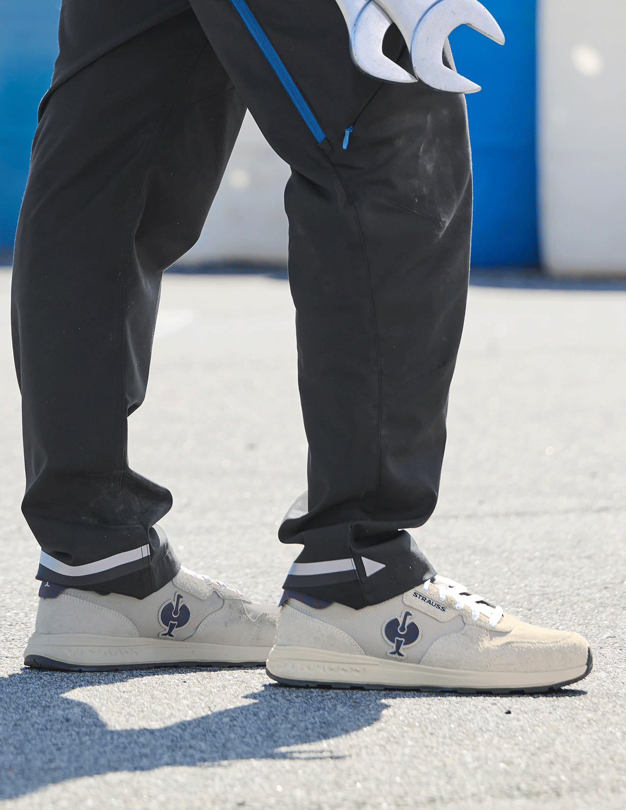 Person wearing black pants and white sneakers with a logo on a concrete surface.