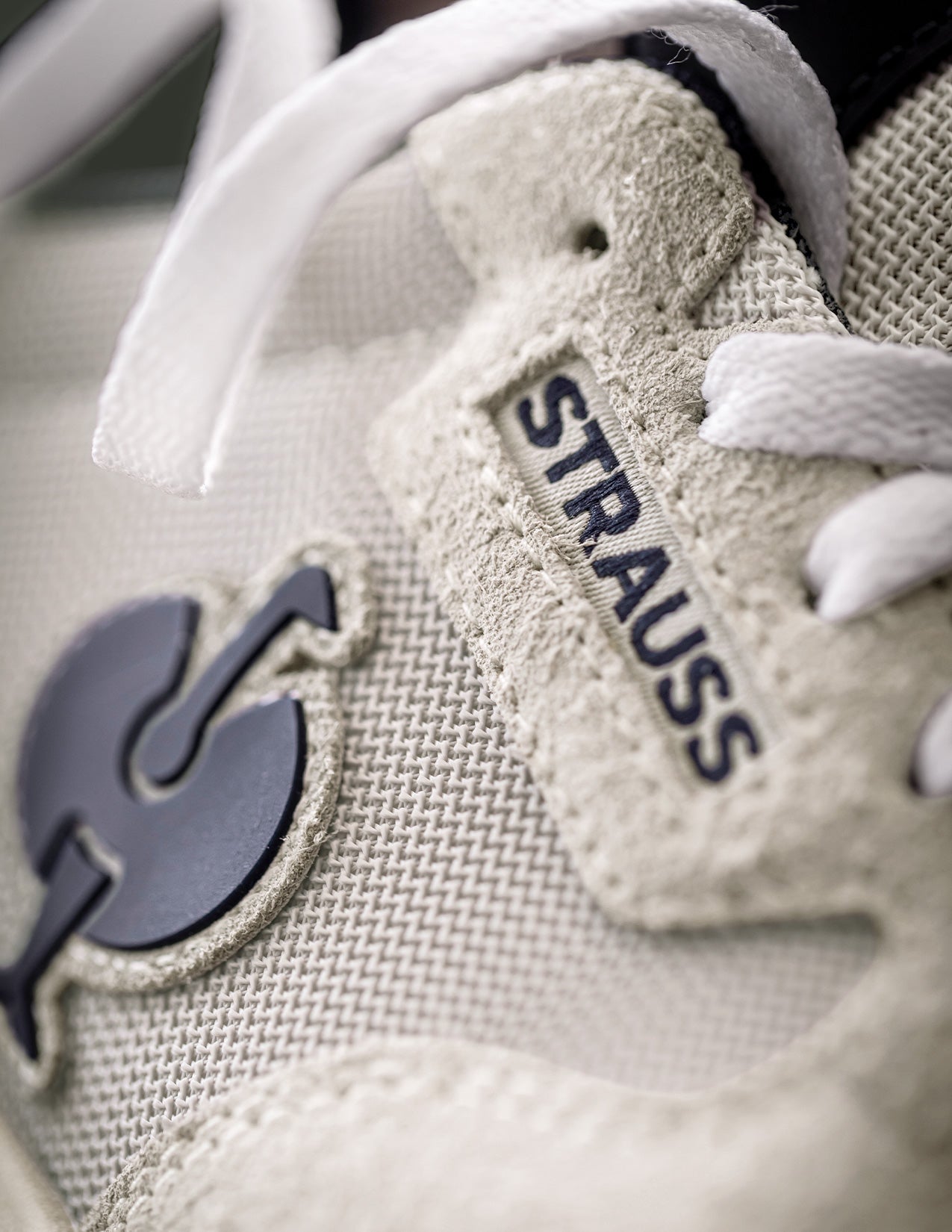 Close-up of a beige sneaker with 'Strauss' branding and logo.