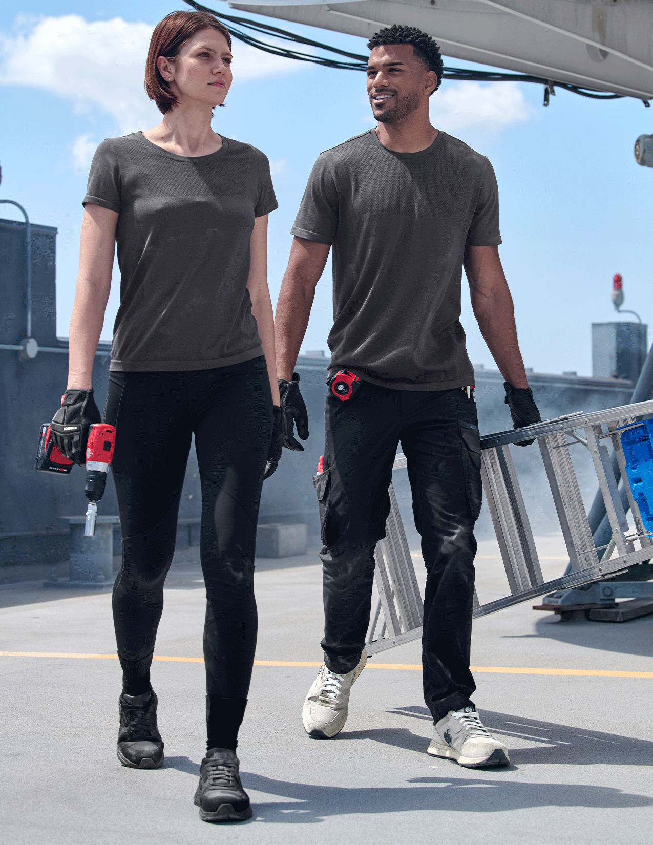 Two people wearing matching dark gray t-shirts and black pants on a rooftop.