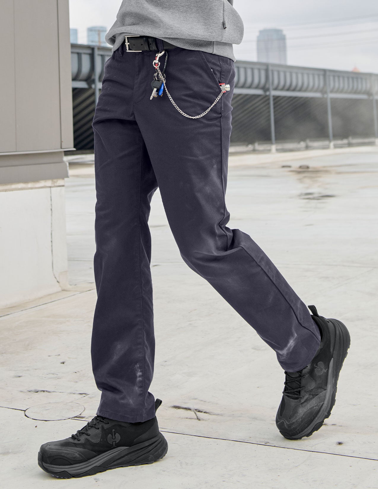 Person wearing dark pants and black shoes on a rooftop with cityscape in the background