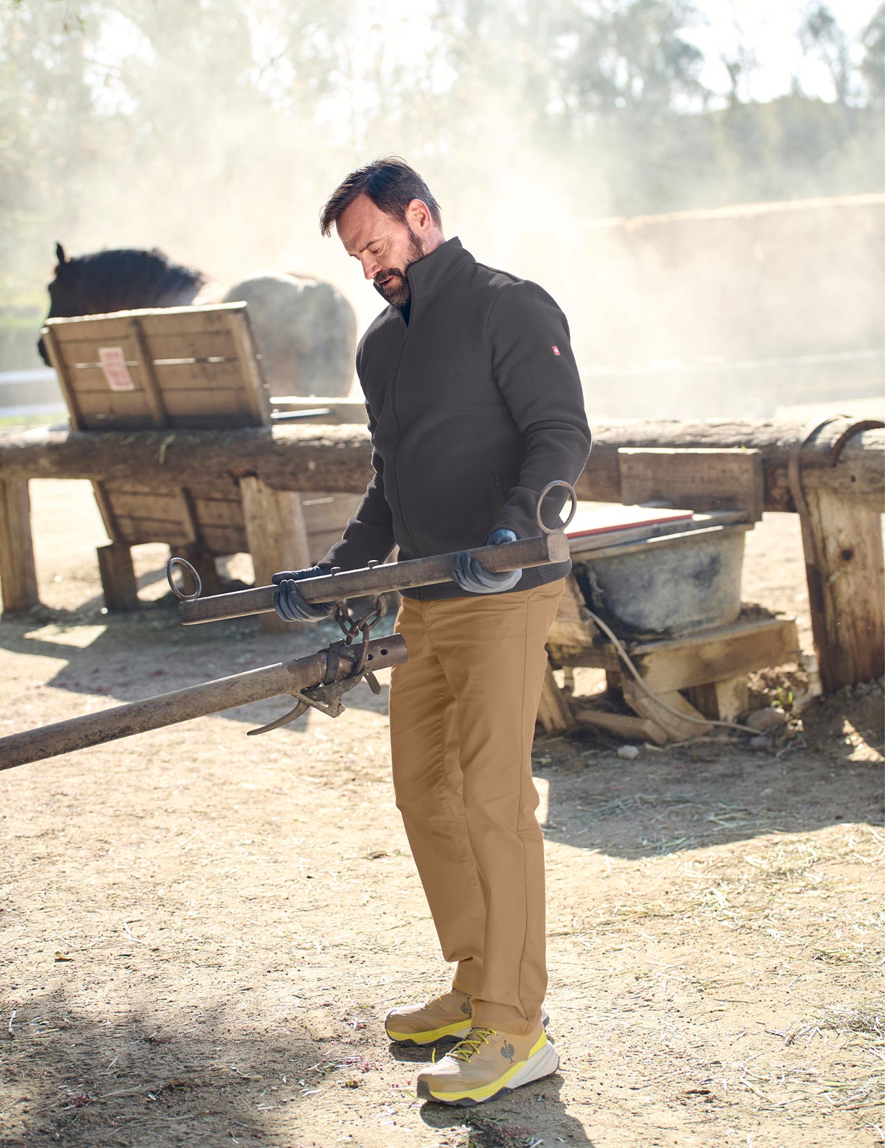 Man holding a long tool near a horse in an outdoor setting