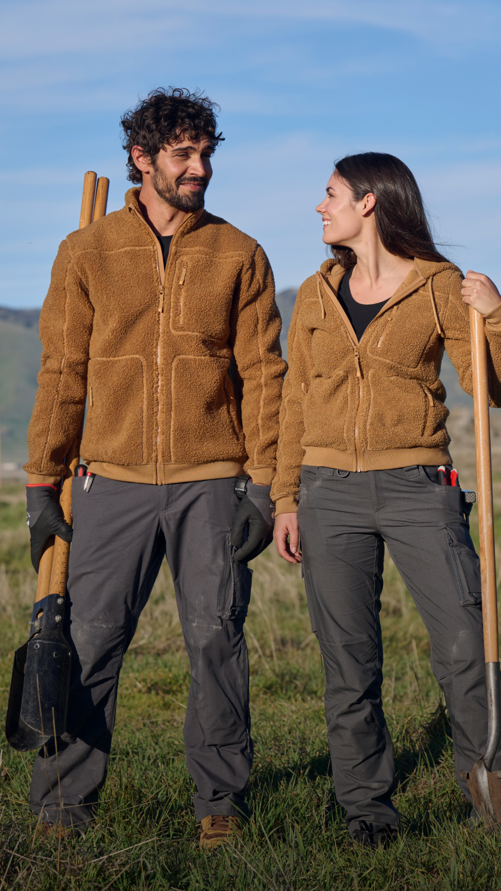 A man and a woman look at each other in a field while wearing workwear