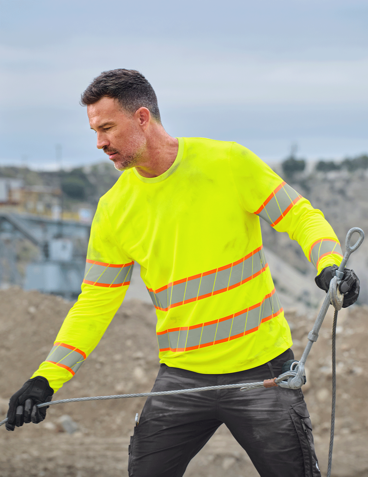 Person wearing a high-visibility safety long sleeve holding equipment outdoors.