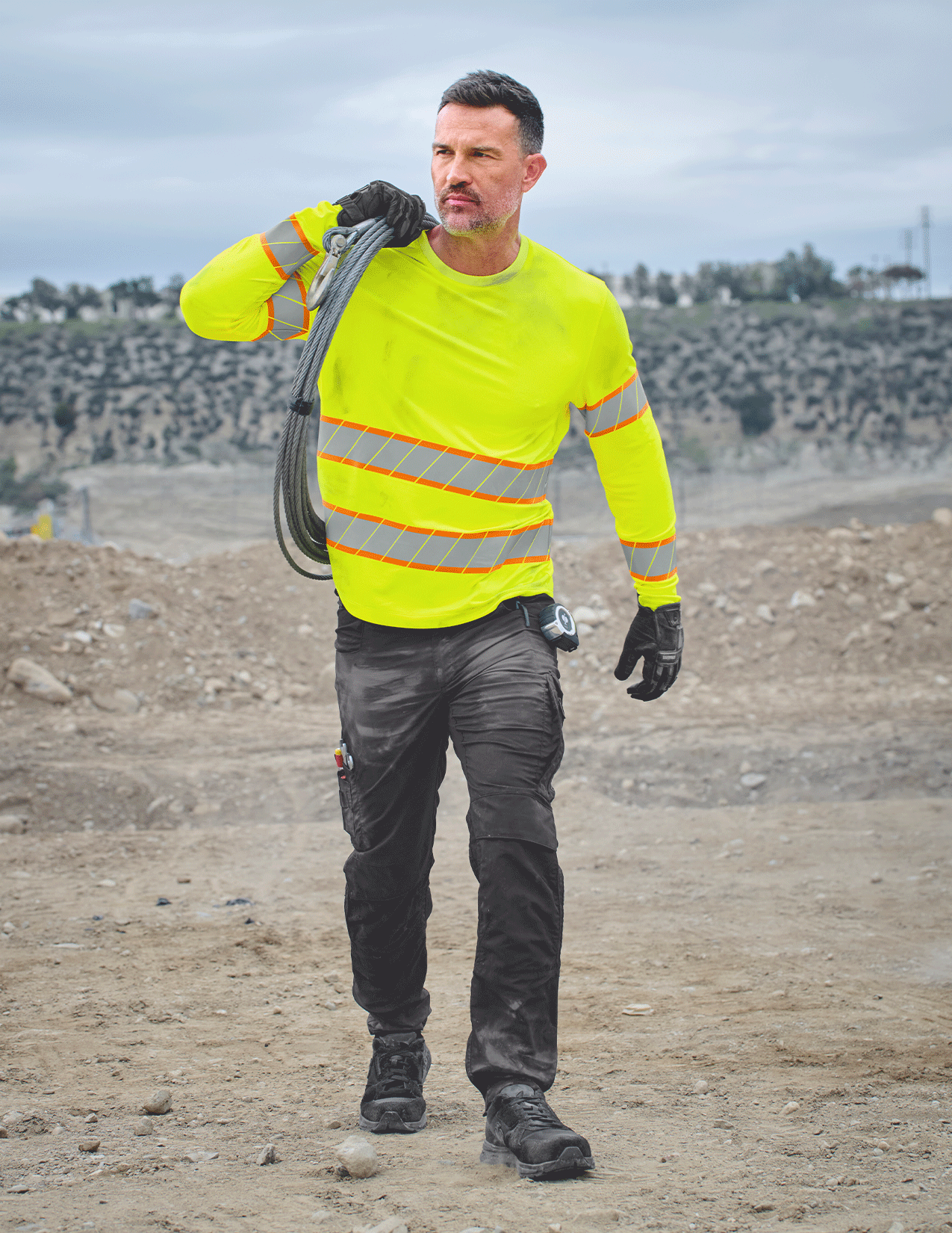 Person wearing a high-visibility safety jacket holding a cable on a construction site.