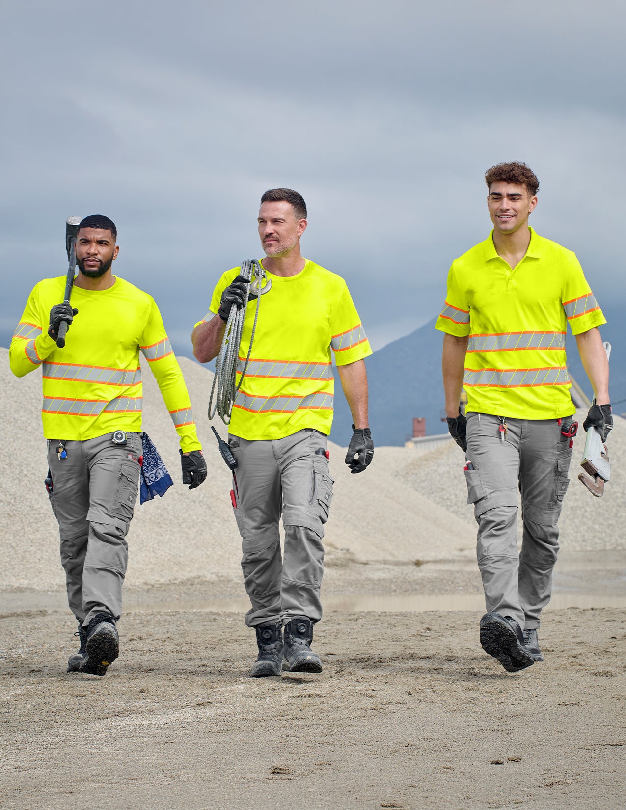 Three workers in high-visibility clothing walking outdoors on a construction site.