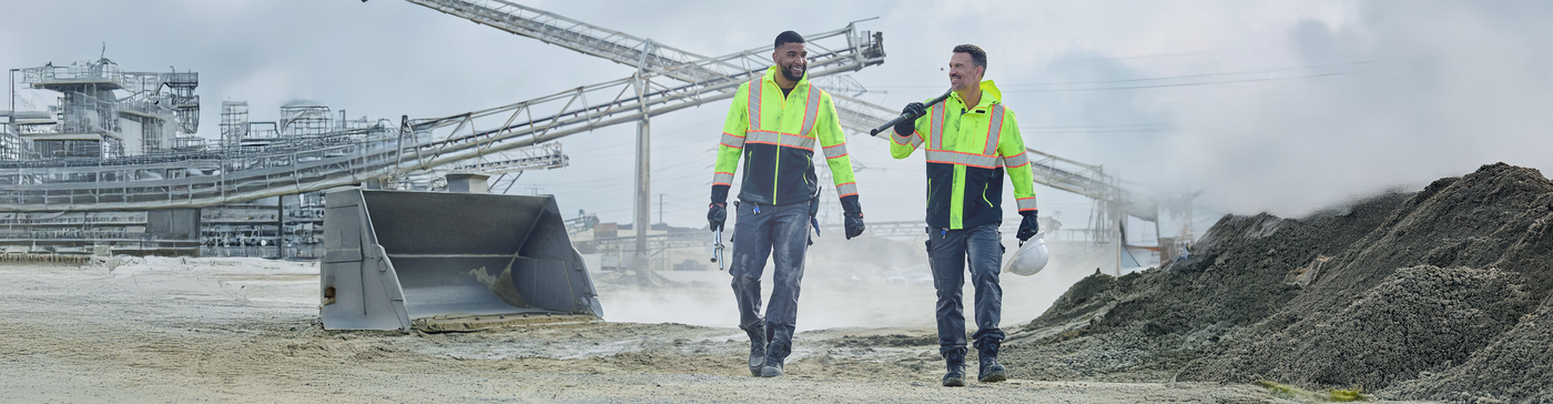 Men in high visibility work jackets walk around quarry.