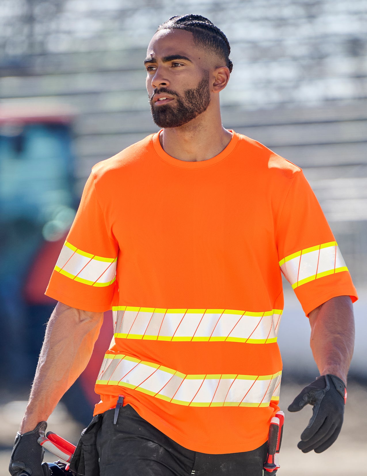 Person wearing an orange safety shirt with reflective stripes outdoors