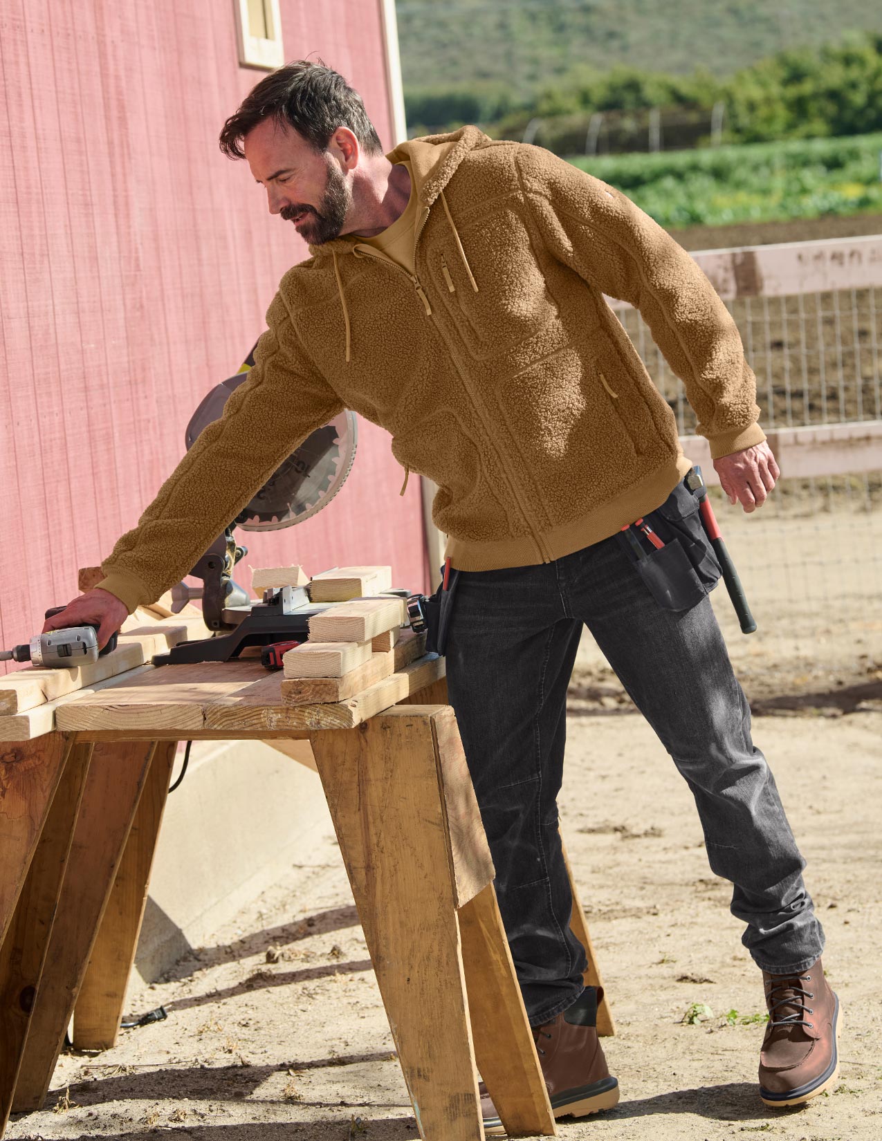 Man working on a wooden table outdoors with a red building in the background