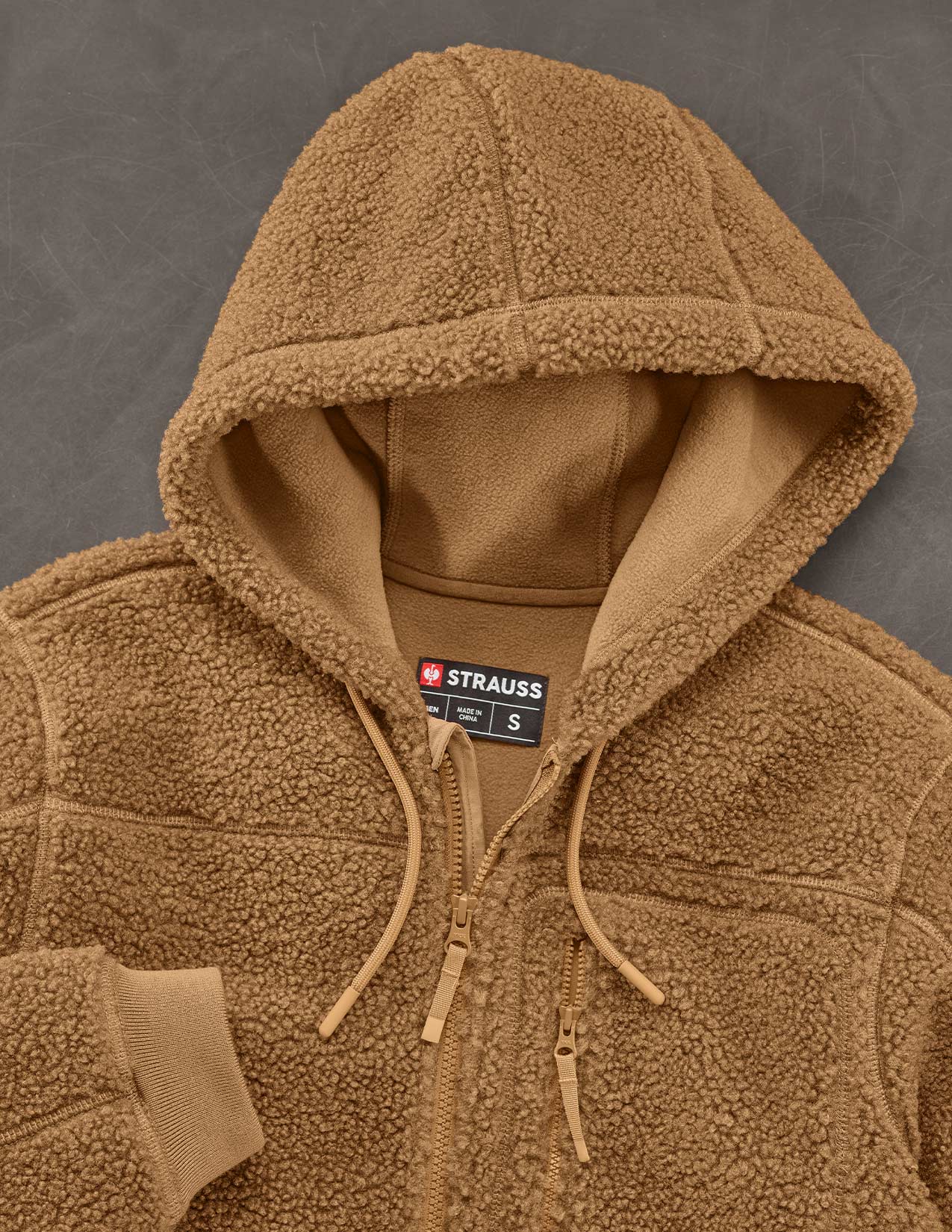 Brown fleece jacket with a visible Strauss label on a gray background