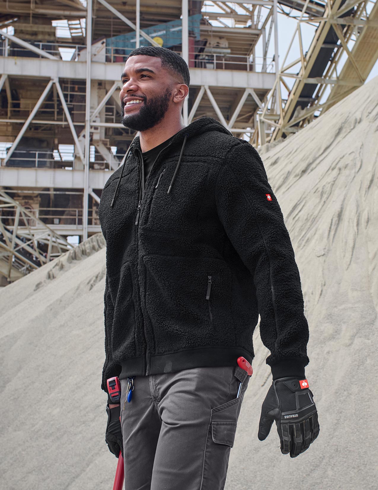 Man wearing a black jacket and gloves in an industrial setting