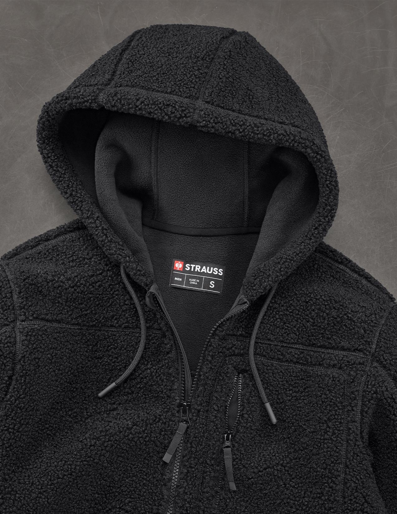 Black fleece jacket with Strauss brand label on a gray background
