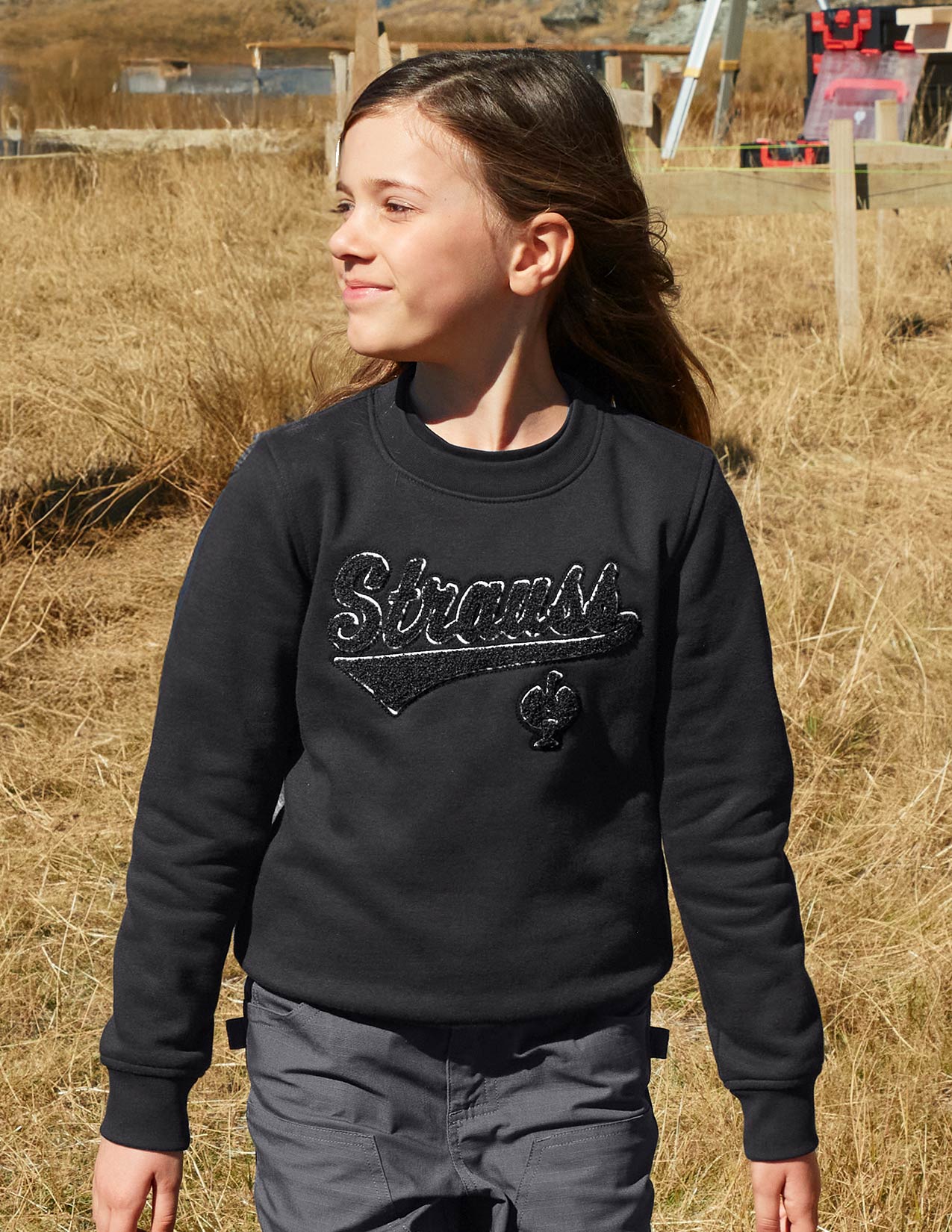 Girl wearing a black sweatshirt with 'Strauss' logo in a field