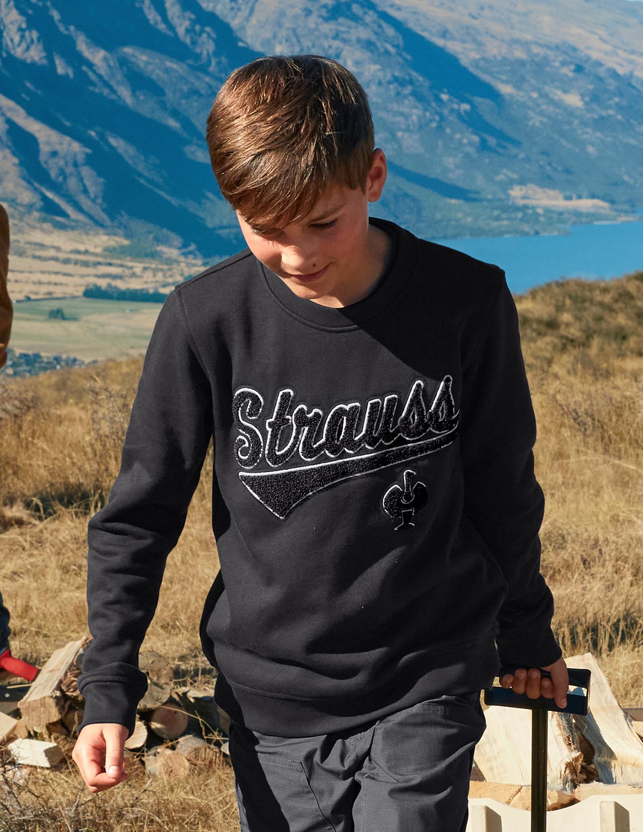 Child wearing a black 'Strauss' sweatshirt with mountains in the background