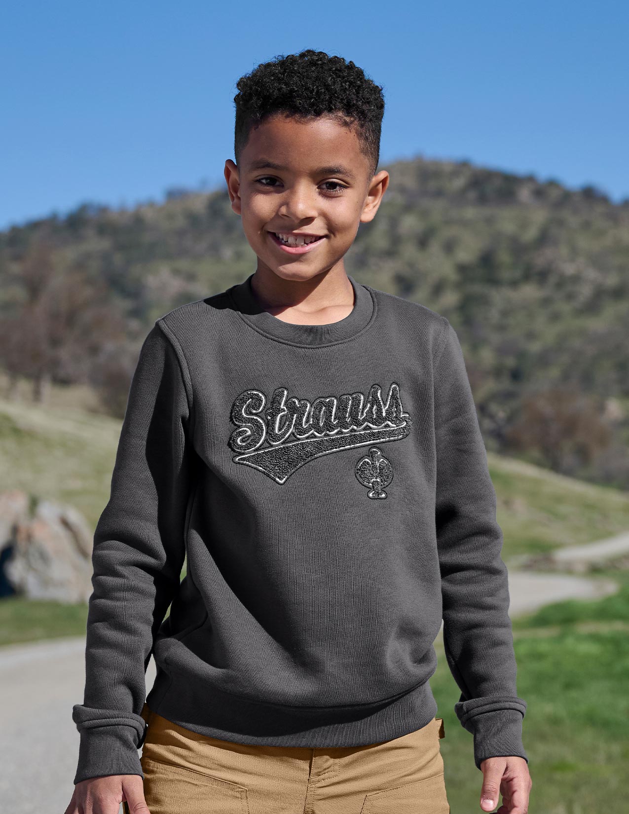 Child wearing a gray sweatshirt with a logo in a natural setting