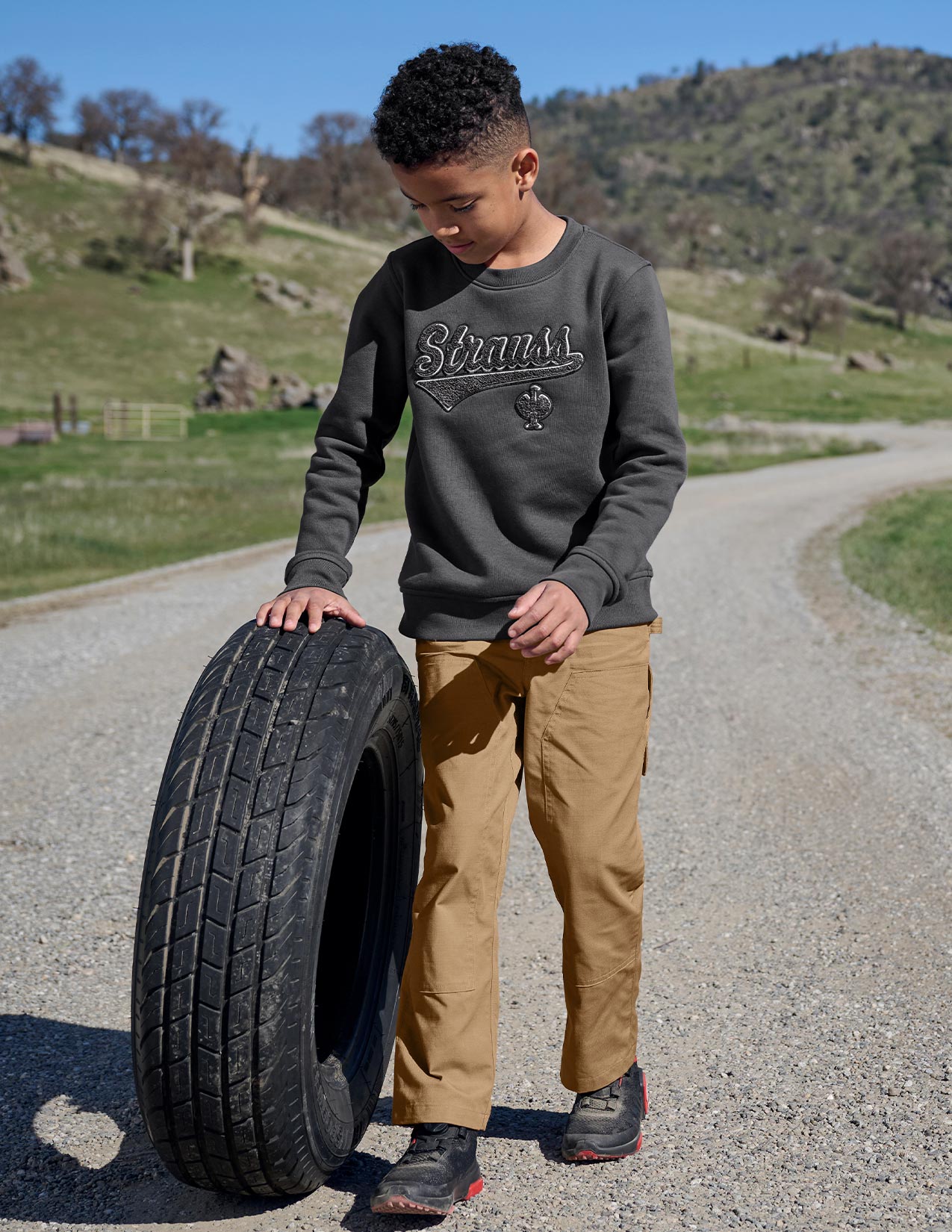 Child holding a tire on a rural road with greenery in the background