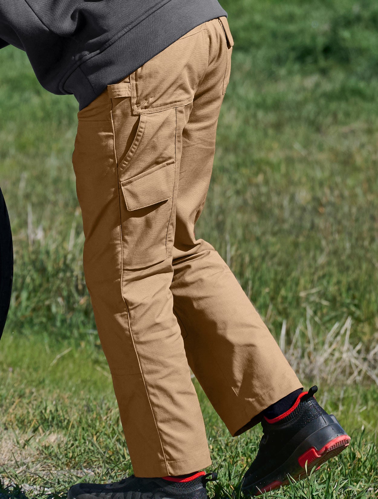 Child wearing beige pants and black boots with red accents on a grassy background