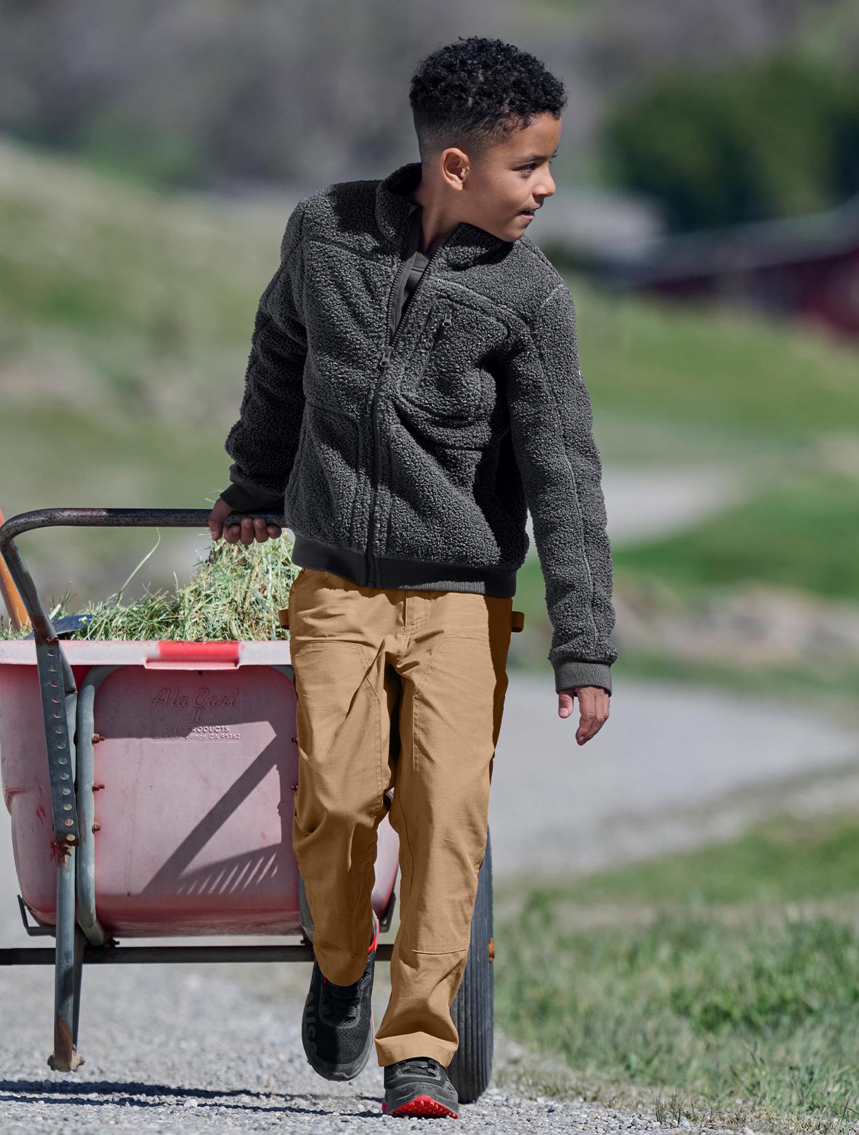 Child walking with a cart outdoors on a grassy area