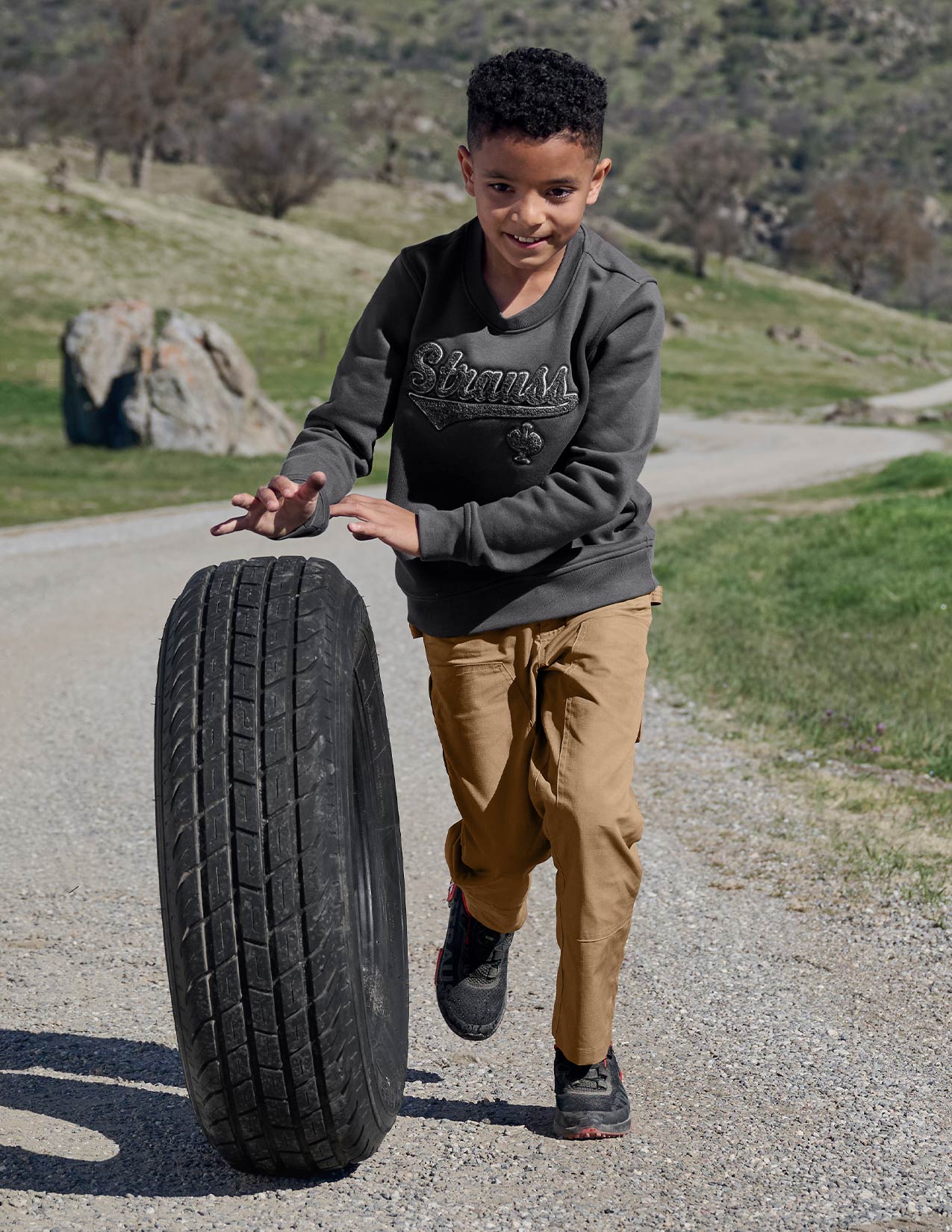 Child playing with a tire on a road with a scenic background