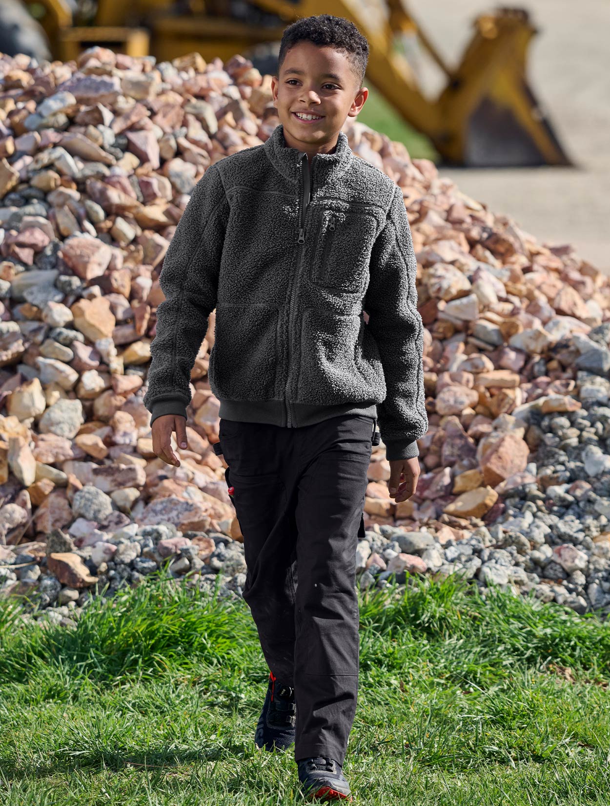 Child wearing a gray fleece jacket standing in front of a pile of rocks