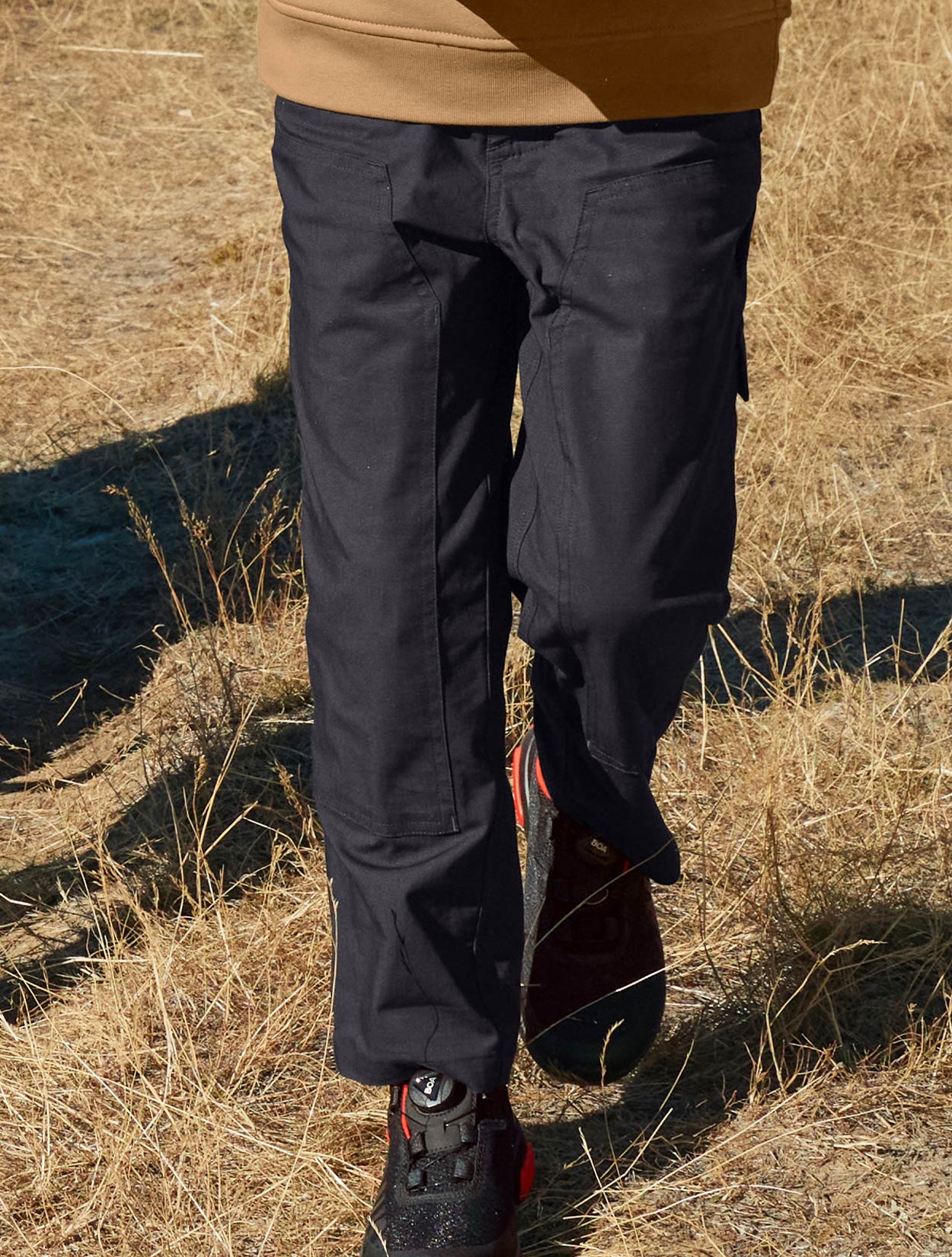 Child standing in a field wearing black pants