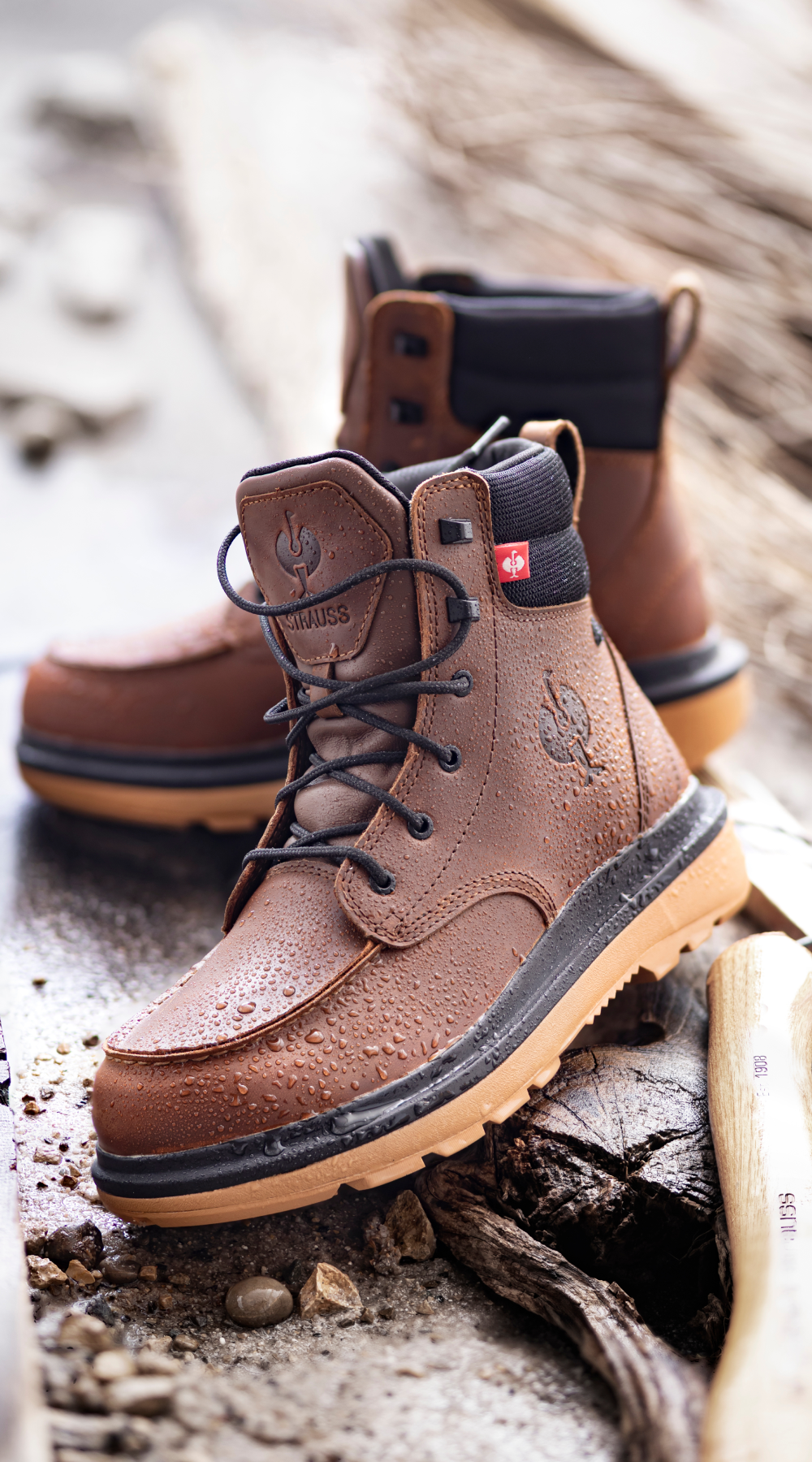 Close-up of brown waterproof leather work boots with water droplets on the surface, placed on a rustic wooden surface next to a hatchet.