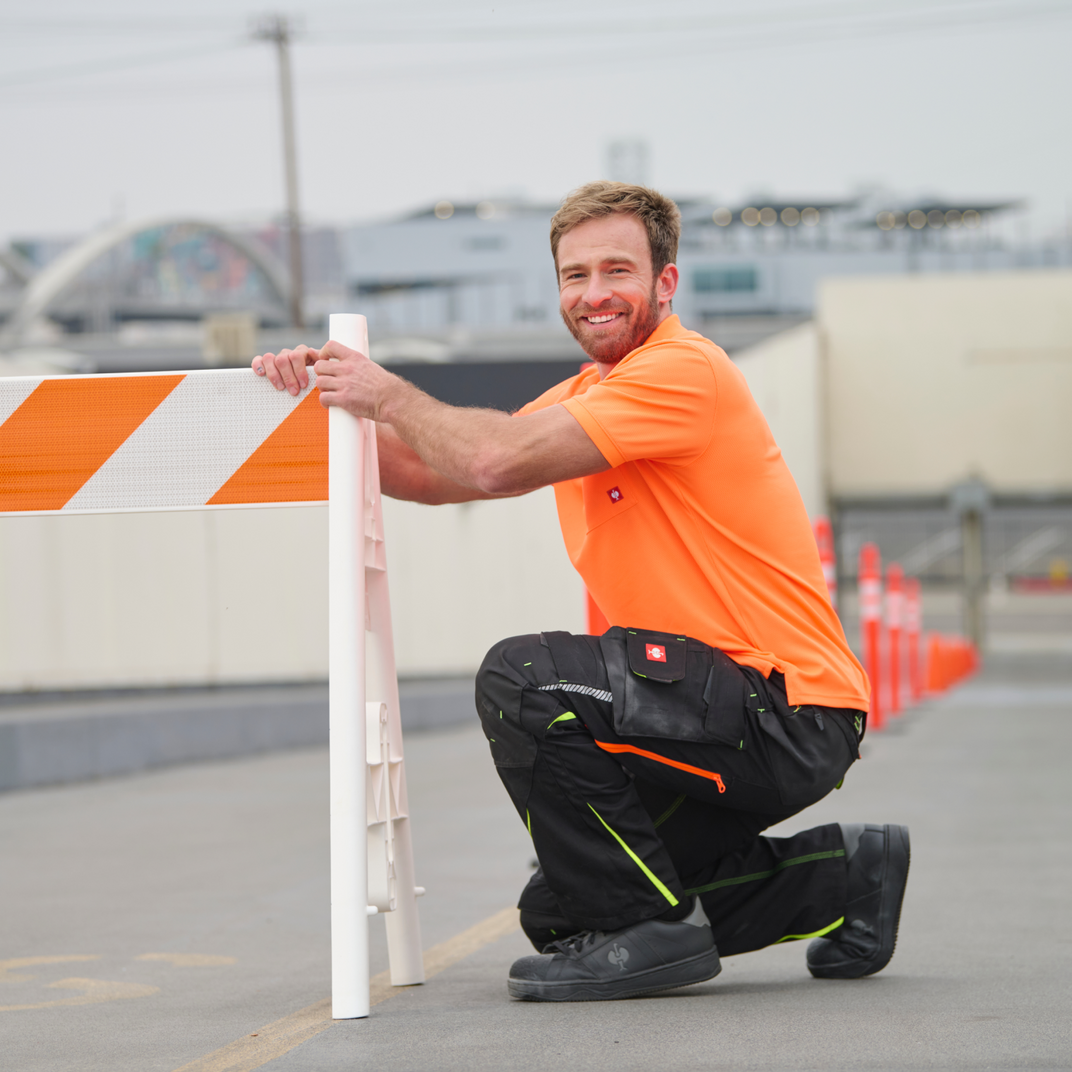 Man in safety gear setting up a roadblock with orange and white barriers.