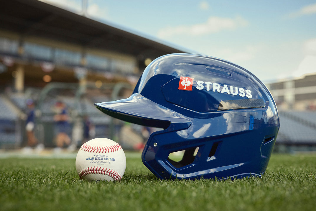 Blue baseball helmet with 'STRAUSS' branding on a grass field