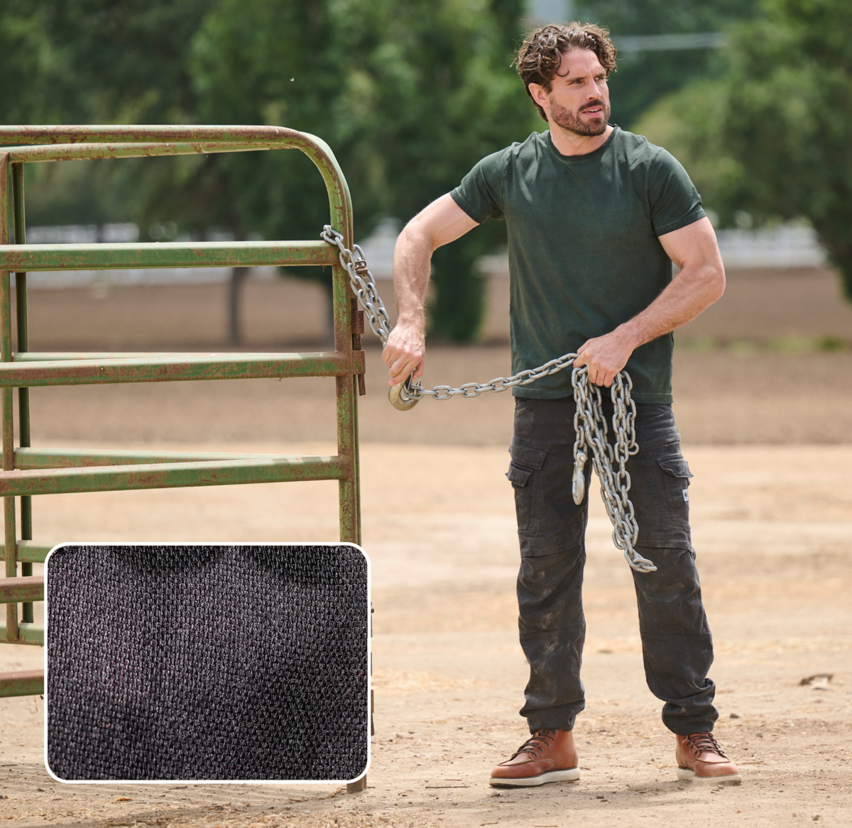 A man in a dark T-shirt and cargo pants chains a metal gate outdoors. An inset shows a close-up of black fabric texture, highlighting the shirt material. Trees and dirt ground are visible in the background.