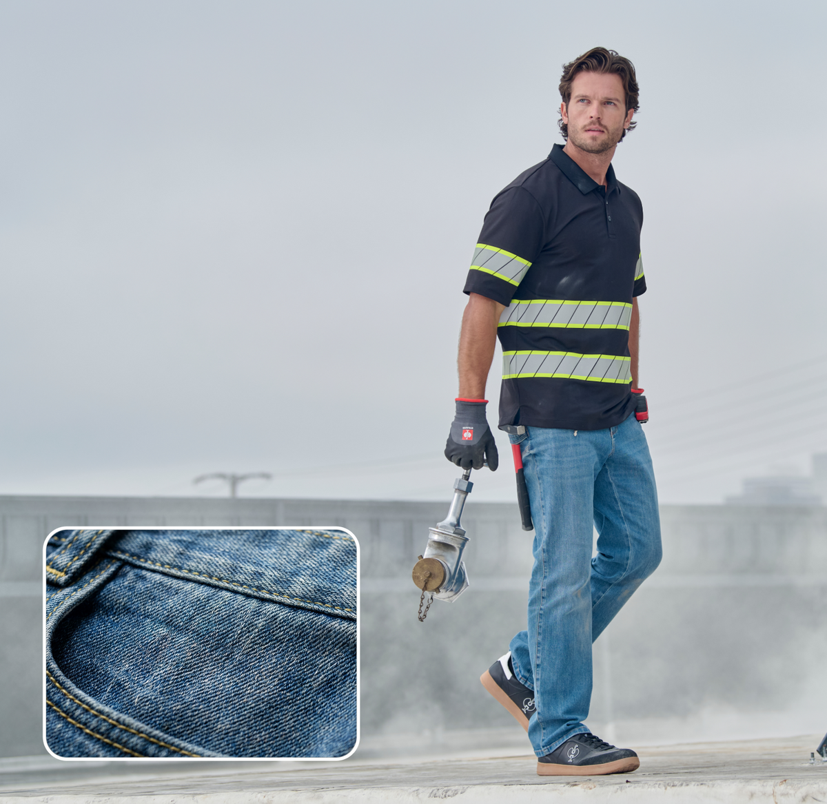 A man in jeans, gloves, and a black shirt with reflective stripes stands outdoors holding a metal tool. Inset: close-up of blue denim fabric with visible stitching. Sky and power lines are visible in the background.