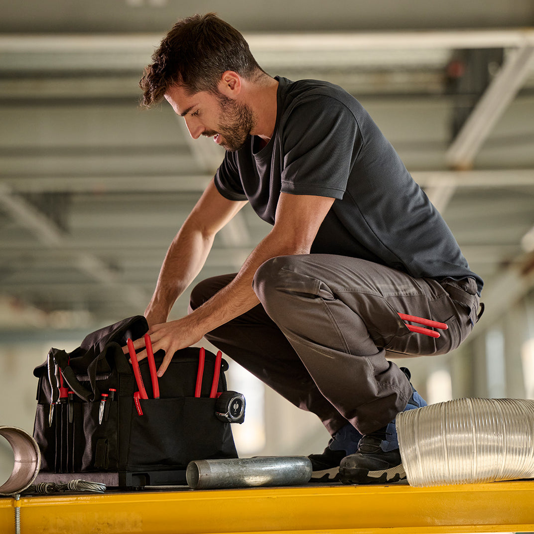 Man in Strauss pants bends down to get something from his tool bag