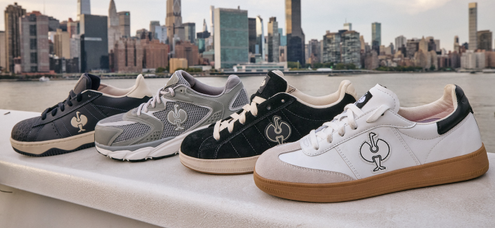 Four safety sneakers with a brand logo displayed on a concrete ledge with a city skyline in the background.