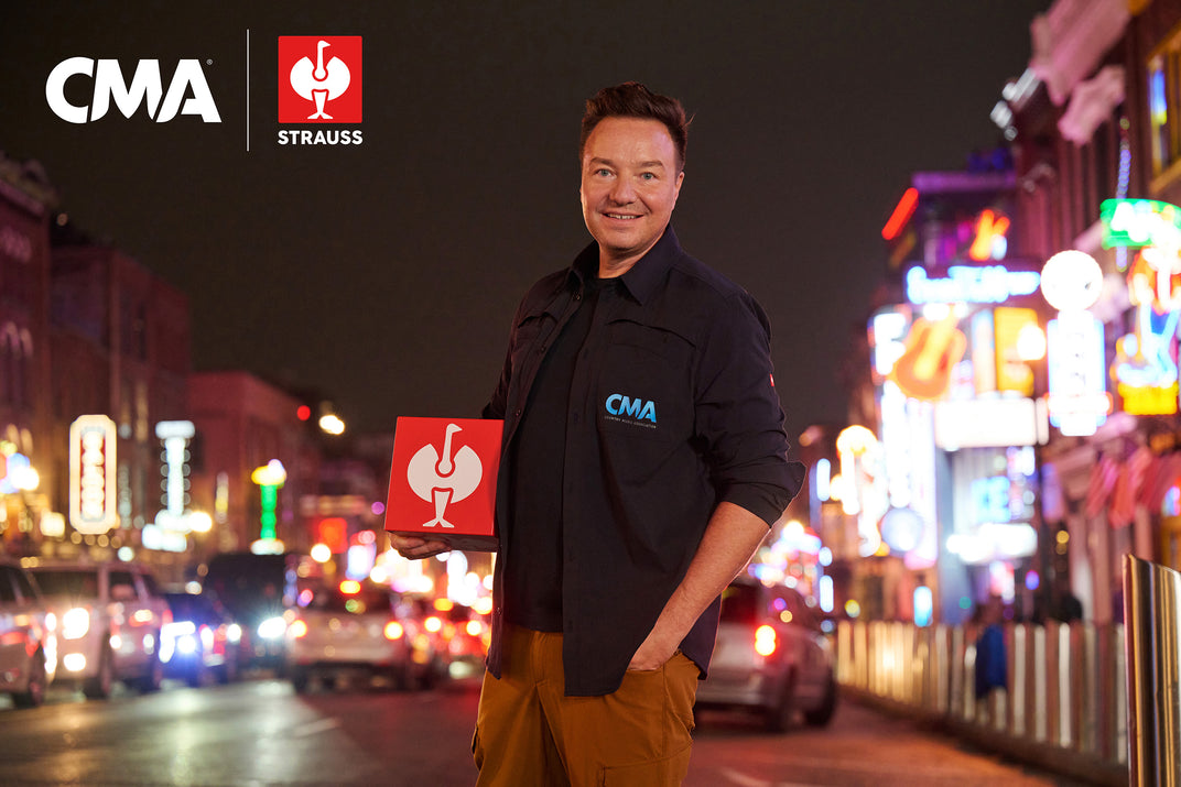 Henning Strauss wearing a CMA Strauss shirt on a neon-lit street at night with a CMA | STRAUSS logo in the upper left