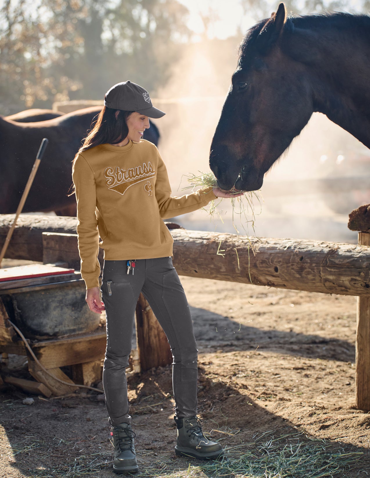 Woman in yellow sweatshirt and gray pants feeding a horse in a rustic setting