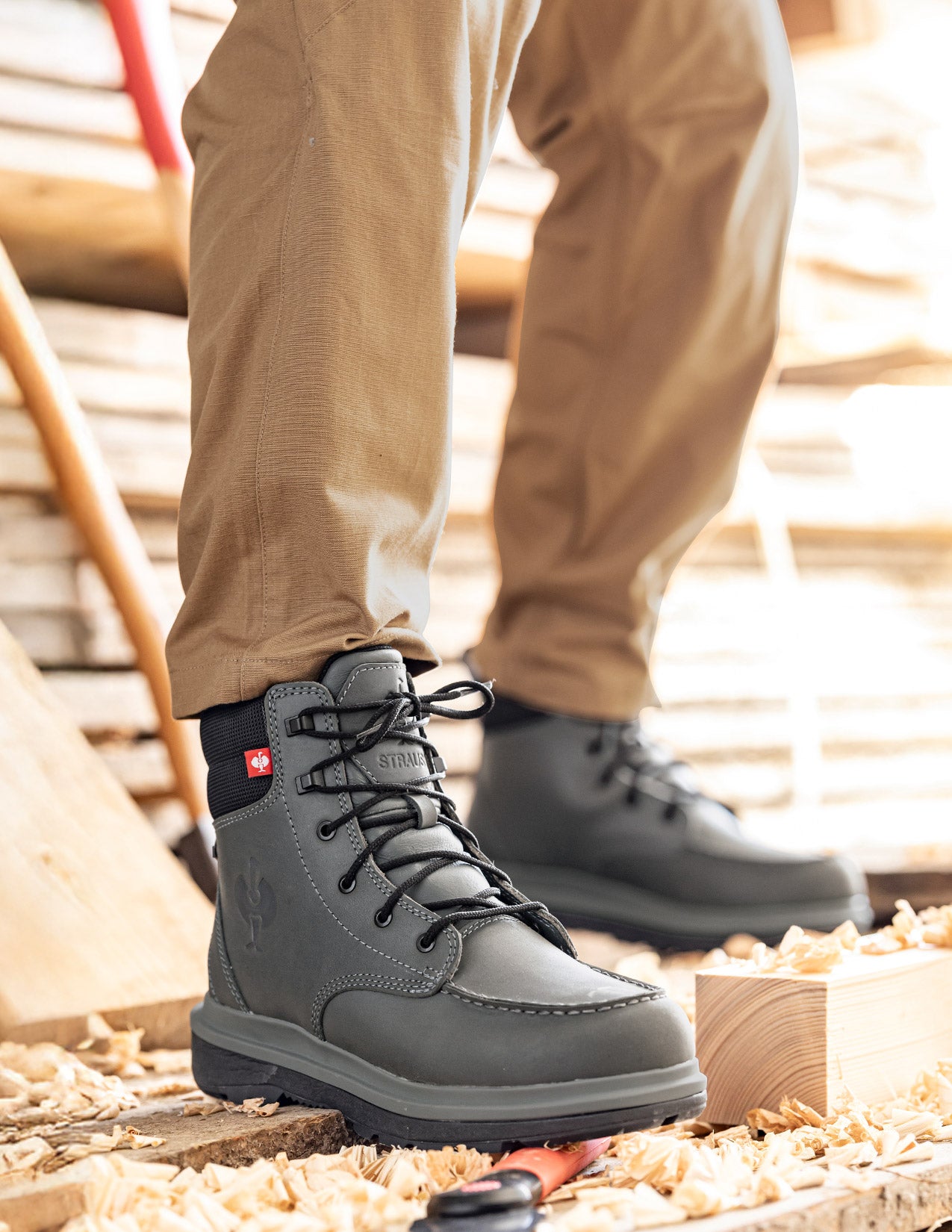 Gray work boots with a brand logo worn by a person on a construction site.