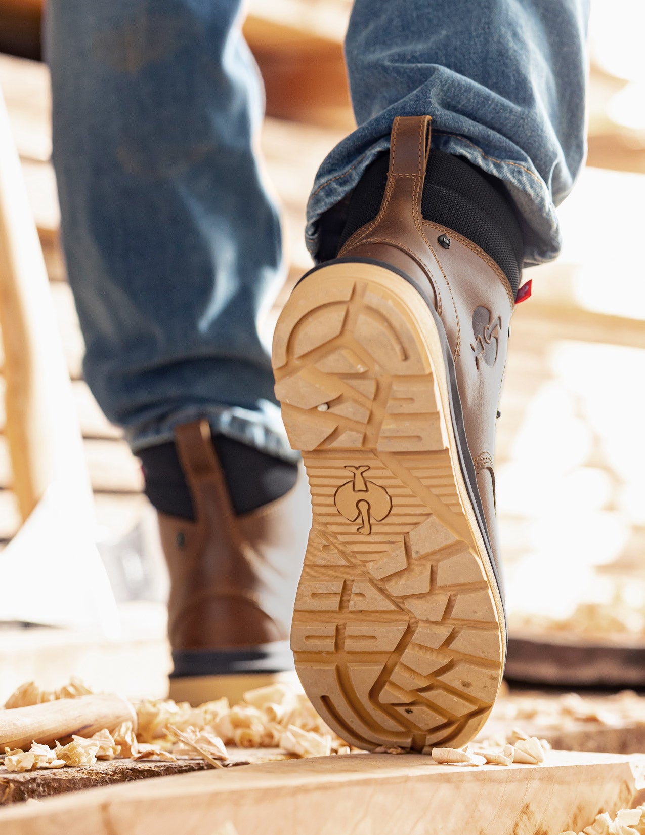 Close-up of a person wearing work boots with a visible brand logo on a wooden floor.