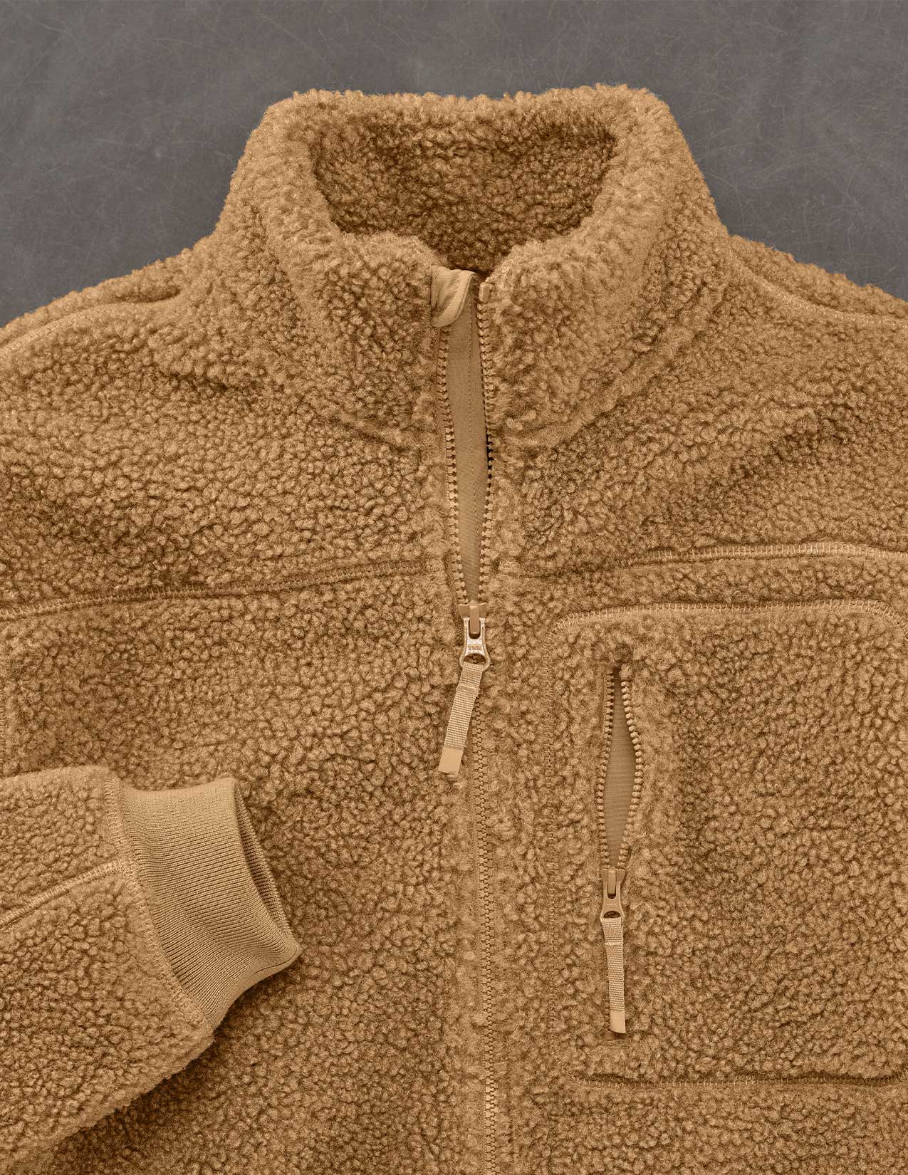 Close-up of a brown fleece jacket with zippers on a gray background