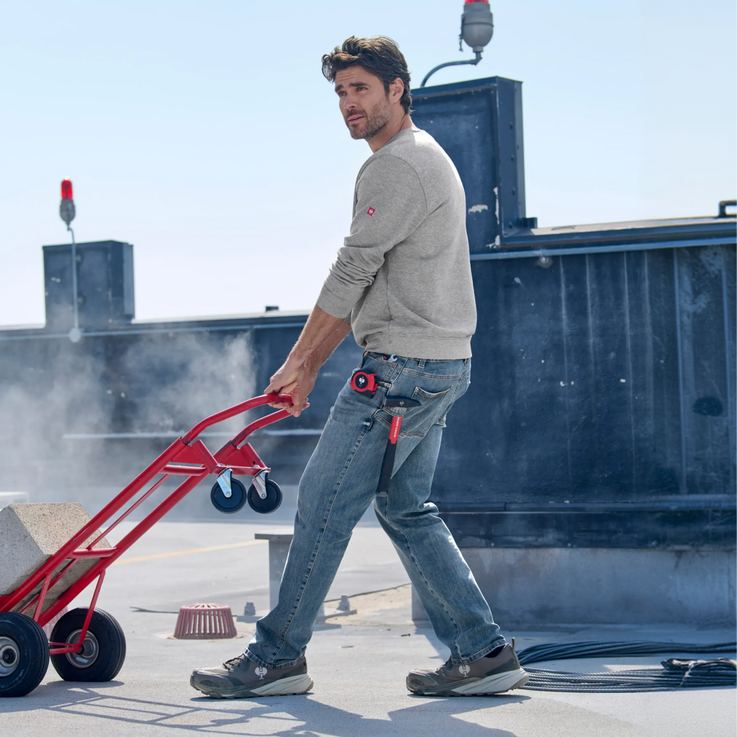 Man pushing a red hand truck on a rooftop with a clear sky.
