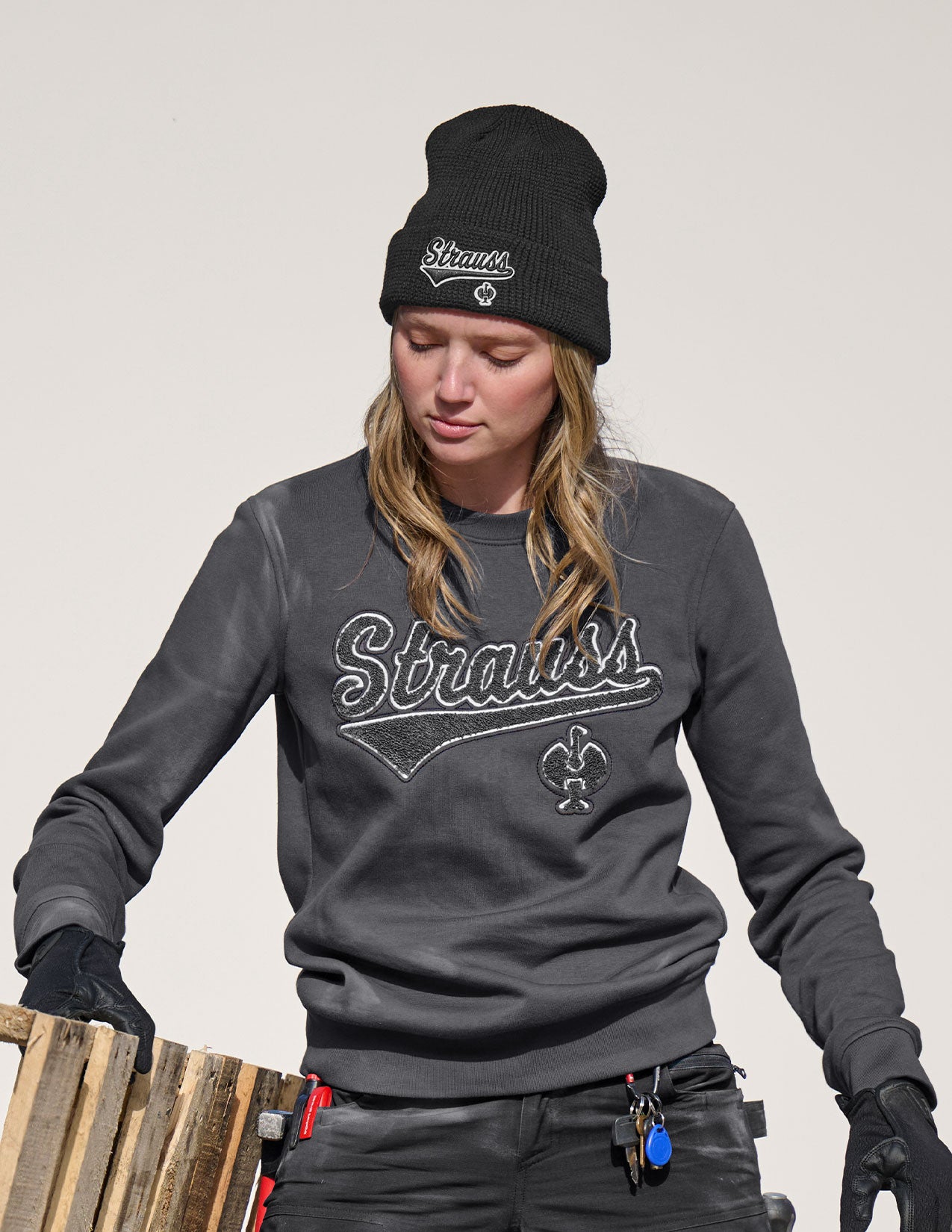 Person wearing a gray sweatshirt with 'Strauss' branding and a black beanie on a plain background