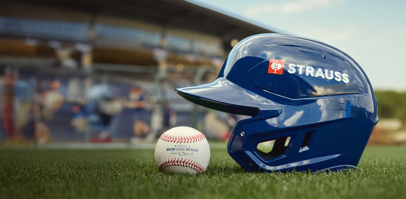 Blue baseball helmet and ball on a grass field with blurred stadium background